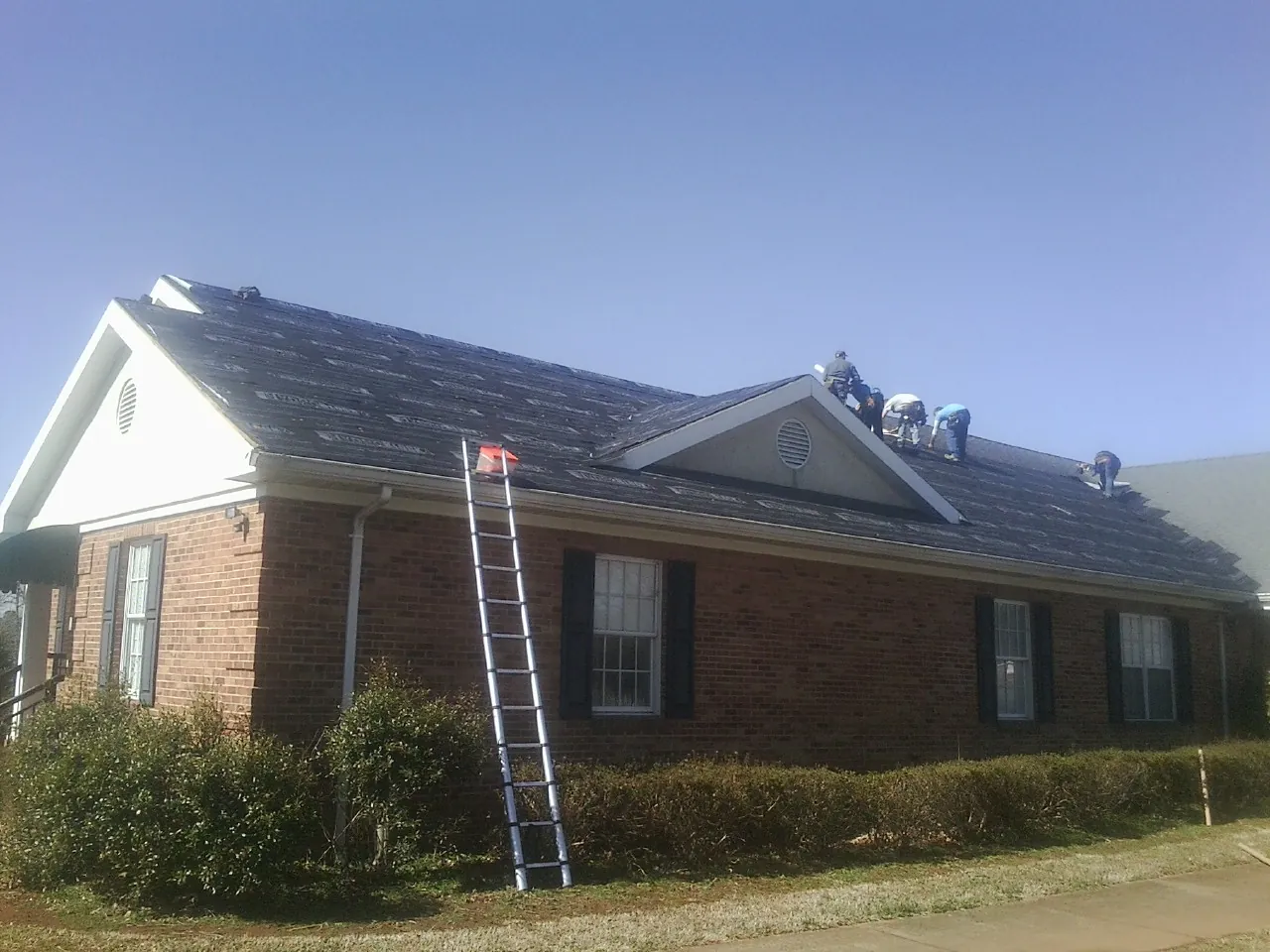 Crew tearing shingles off a brick ranch roof with a ladder set — Emergency Roof Repair work by our crew in Aberdeen Proving Ground