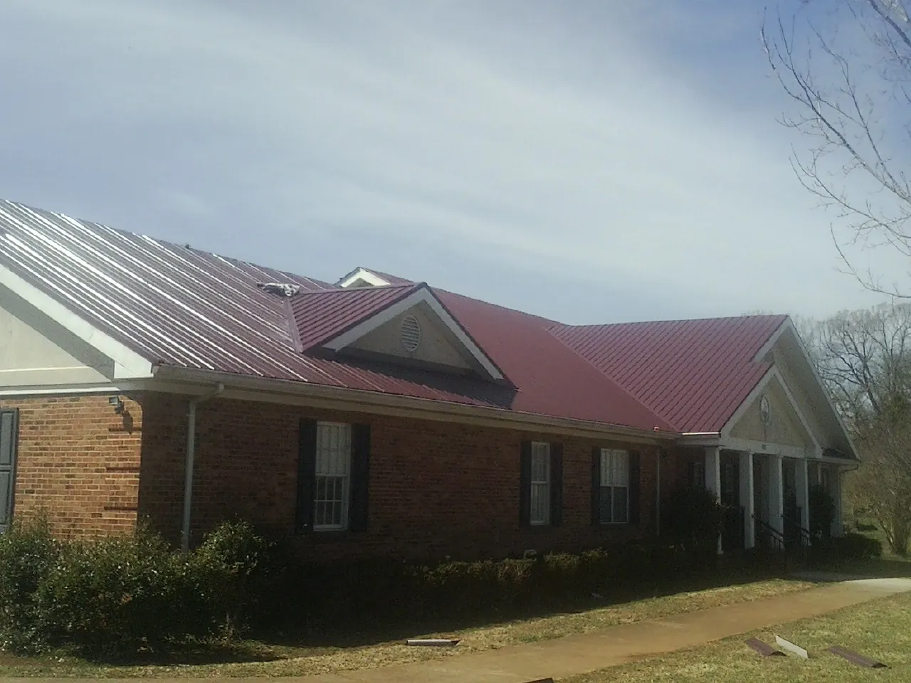 Red metal roof with gabled entries on a long brick building, from a Hail Damage Roof Repair job in Aberdeen Proving Ground