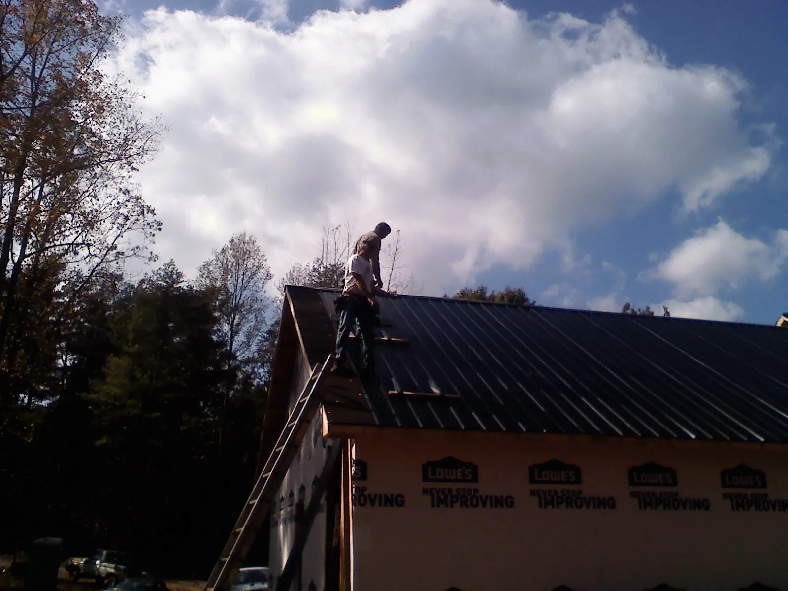 Roofer fastening dark metal panels high against a cloudy sky, from a Roof Inspection job in Aberdeen Proving Ground