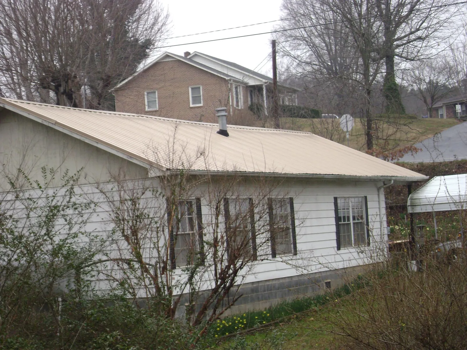 Tan metal roof on a white sided house set into a hillside — Commercial Roofing by Roofing Brothers in Aberdeen Proving Ground